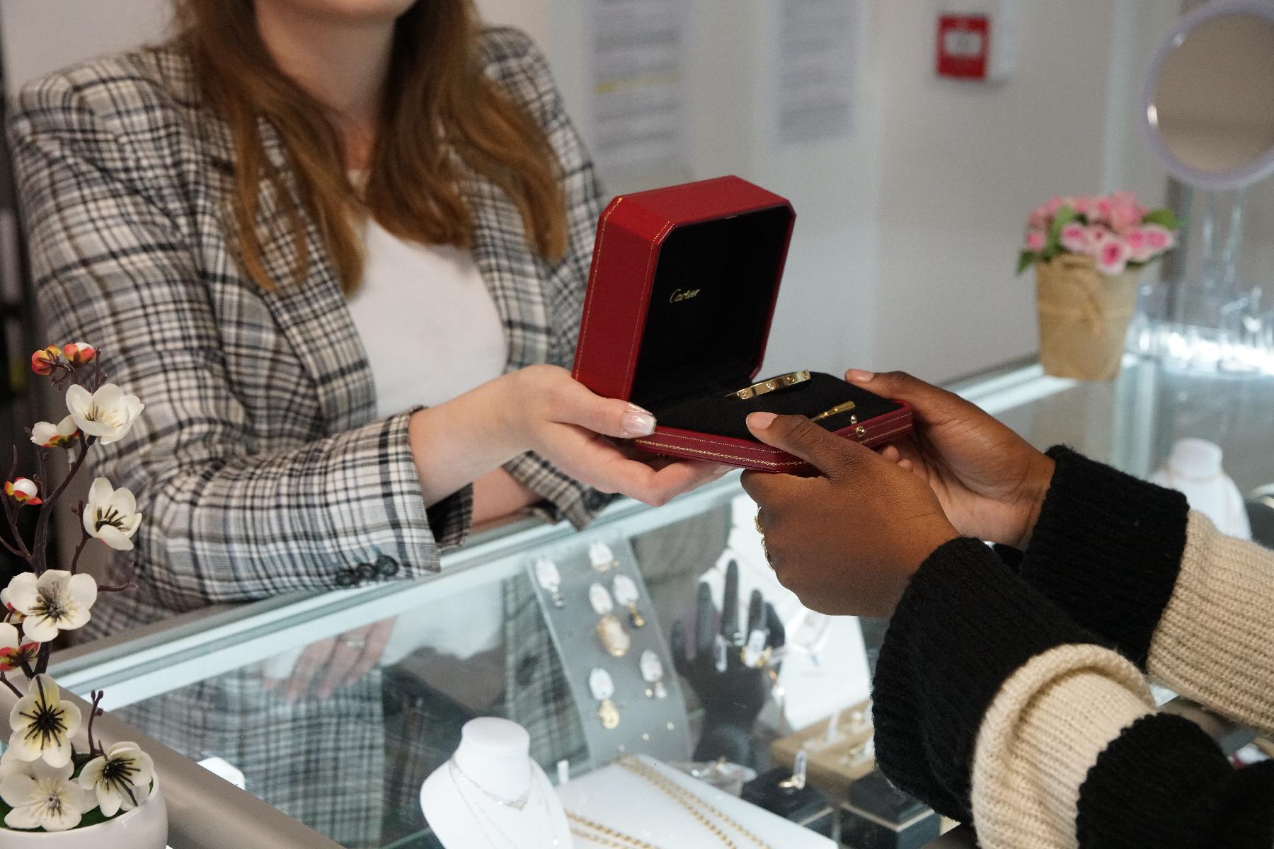 Une vendeuse passe une boite avec un bijoux à un client